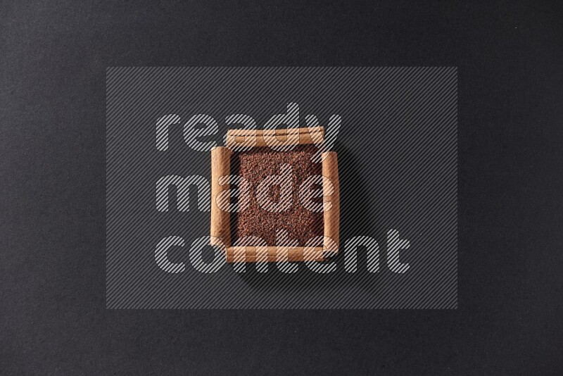 A single square of cinnamon sticks full of garden cress on black flooring