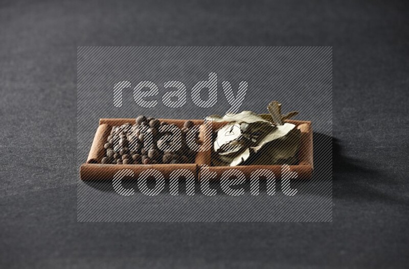 مربعان من أعواد القرفة ممتلئان ببهار الفلفل الحلو وأوراق الغار علي خلفية سوداء