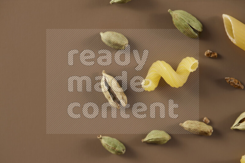 Raw pasta with different ingredients such as cherry tomatoes, garlic, onions, red chilis, black pepper, white pepper, bay laurel leaves, rosemary and cardamom on beige background
