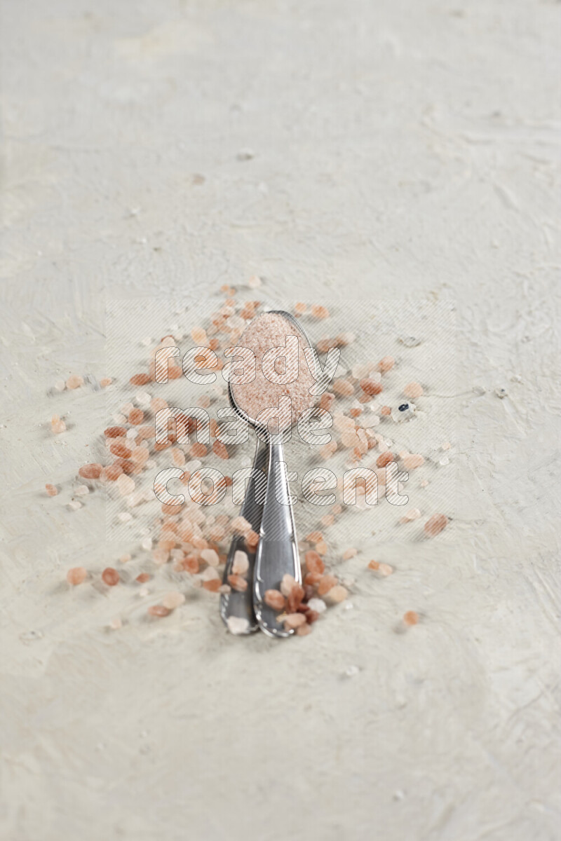 2 metal spoons filled with fine table salt and fine pink himalayan salt on white background