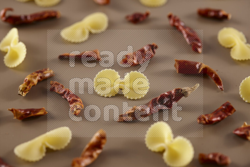 Raw pasta with different ingredients such as cherry tomatoes, garlic, onions, red chilis, black pepper, white pepper, bay laurel leaves, rosemary and cardamom on beige background