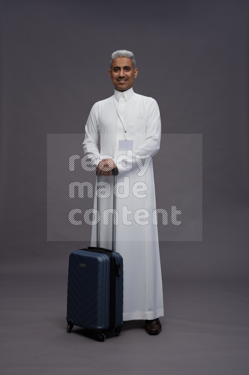 Saudi man wearing thob with neck strap employee badge standing holding bag on gray background