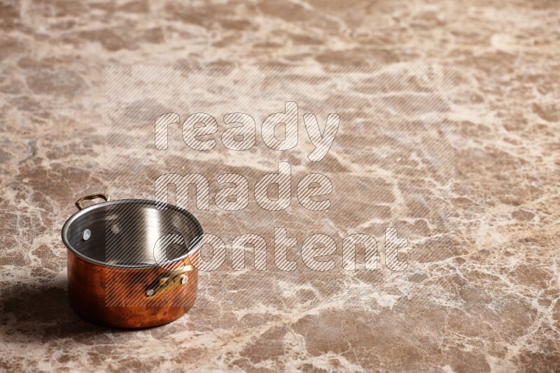 A small copper pot on beige marble background