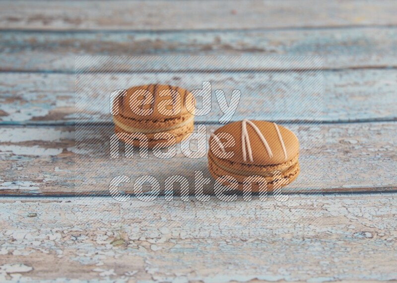 45º Shot of of two assorted Brown Irish Cream, and light brown Almond Cream macarons next to each other on light blue background