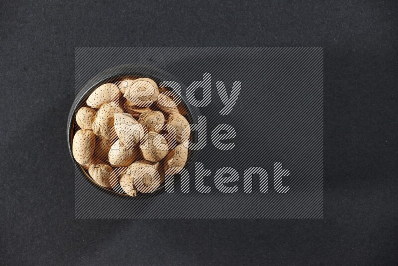 A black pottery bowl full of almonds on a black background in different angles