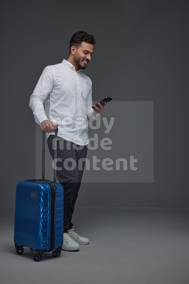 A man wearing smart casual holding luggage eye level on a gray background