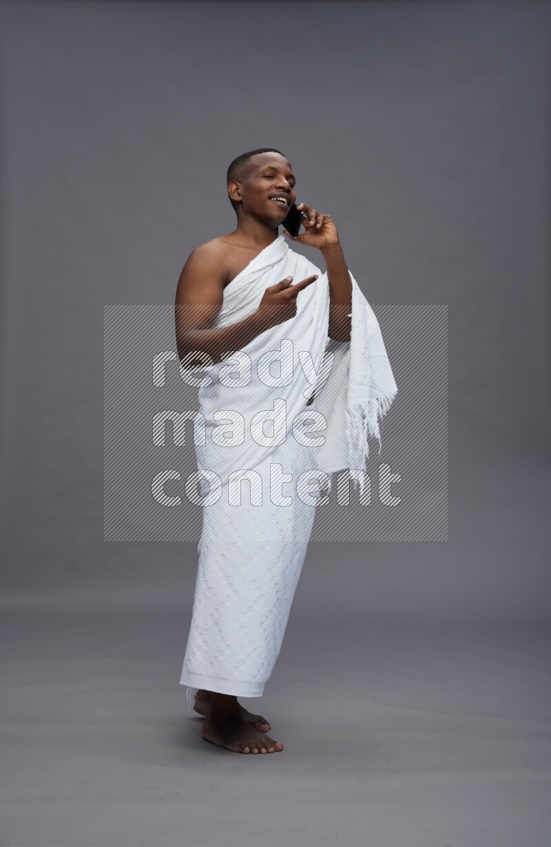 A man wearing Ehram Standing talking on phone on gray background
