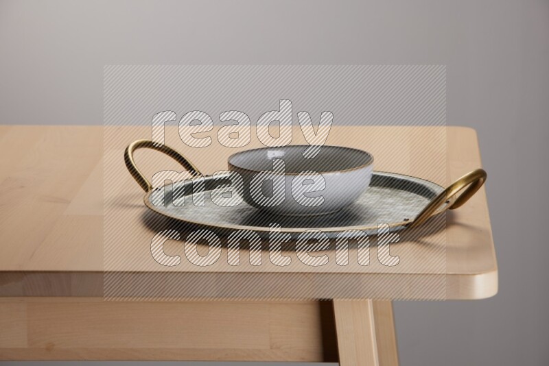 multicolored bowl placed on a rounded stainless steel tray with golden handels on the edge of wooden table