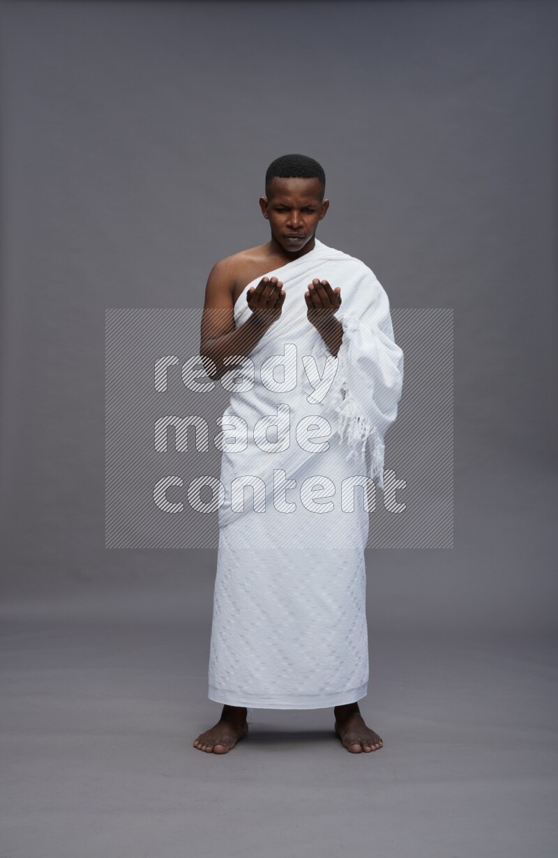 A man wearing Ehram Standing dua'a on gray background
