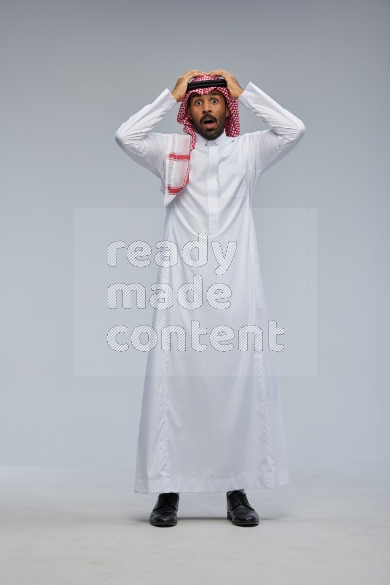 Saudi man Wearing Thob and shomag standing interacting with the camera on Gray background