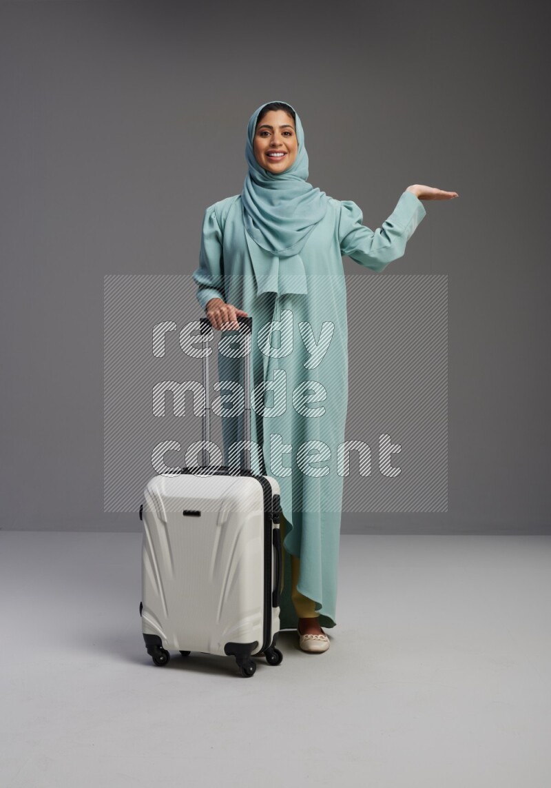 Saudi Woman wearing Abaya standing holding Travel bag on Gray background