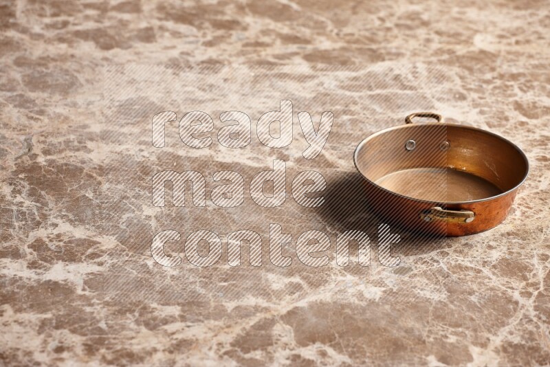 A small copper pan on beige marble background