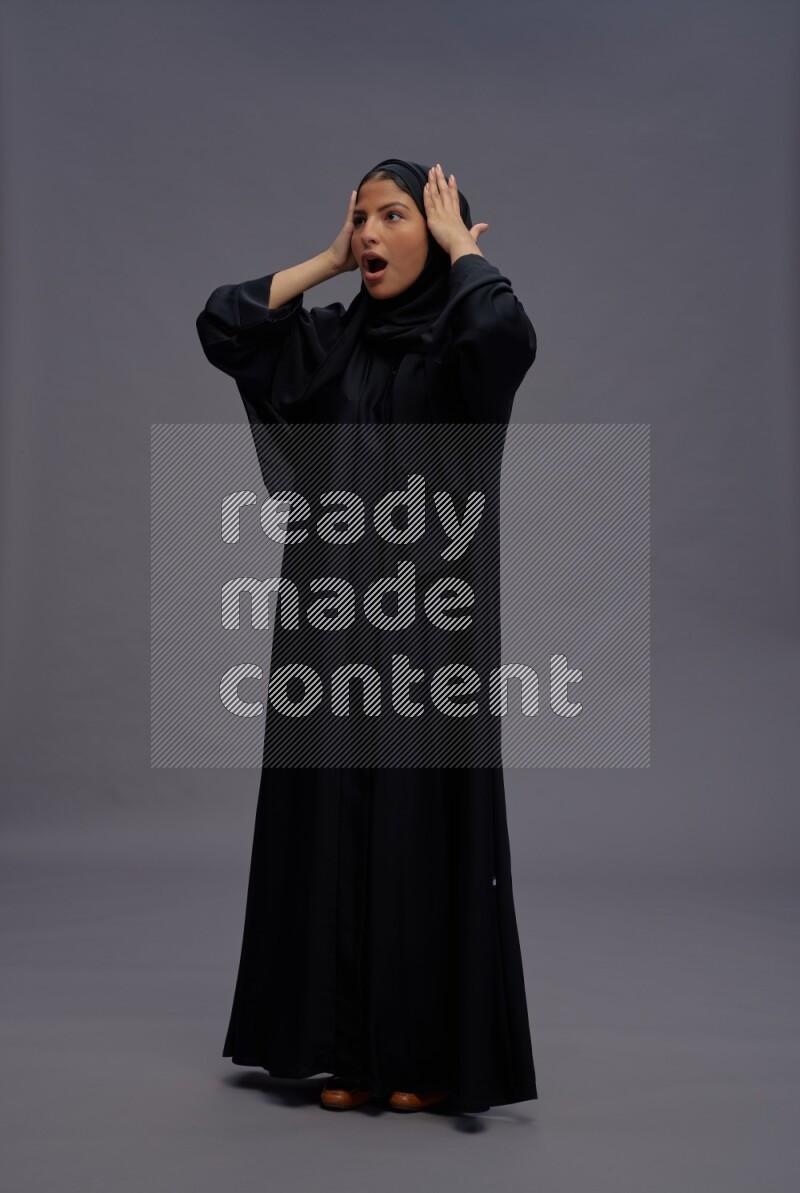 Saudi woman wearing Abaya standing hands behind head on gray background