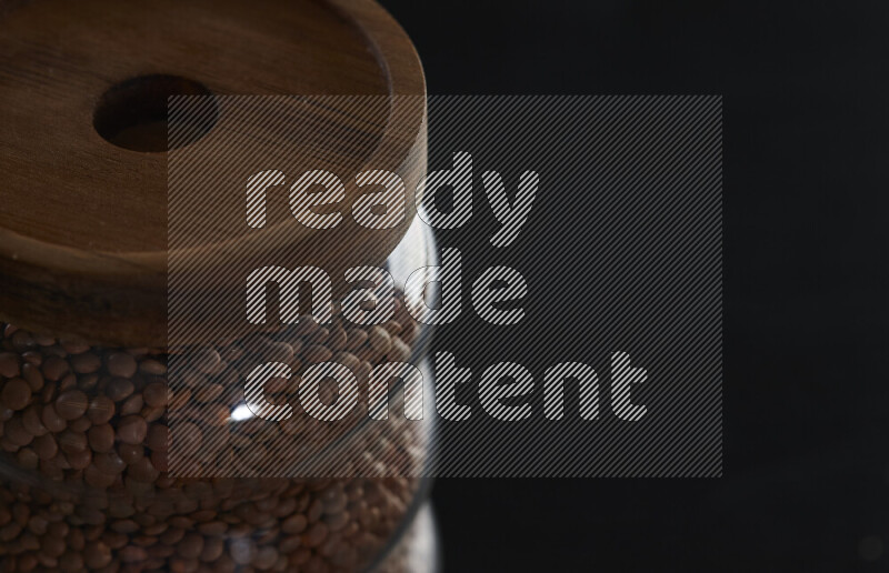 Brown lentils in a glass jar on black background