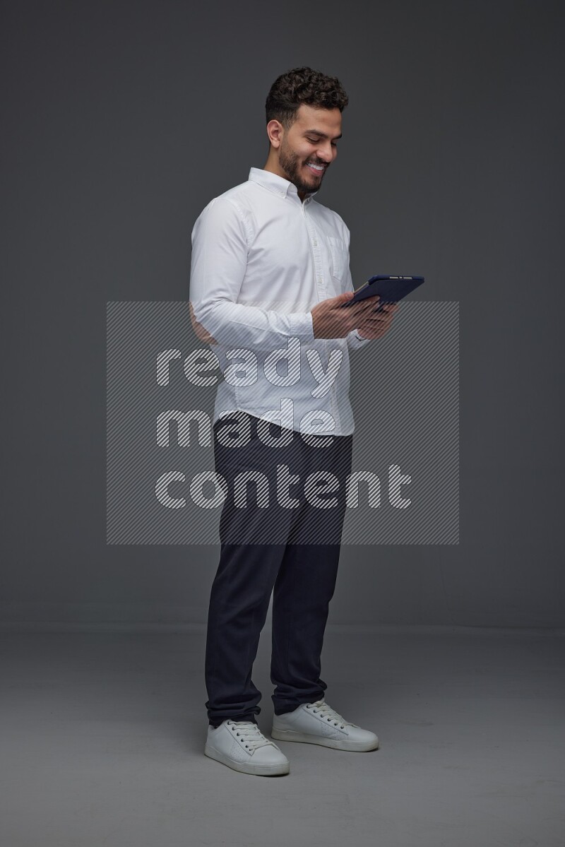 A man wearing smart casual standing and using his tablet eye level on a gray background