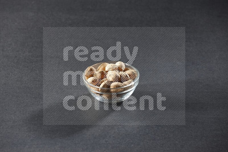 A glass bowl full of almonds on a black background in different angles