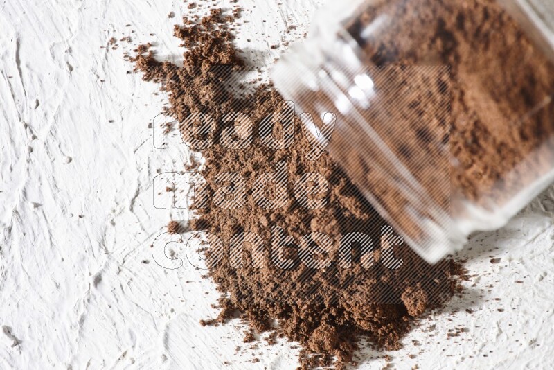 A flipped glass jar full of cloves powder on a textured white flooring
