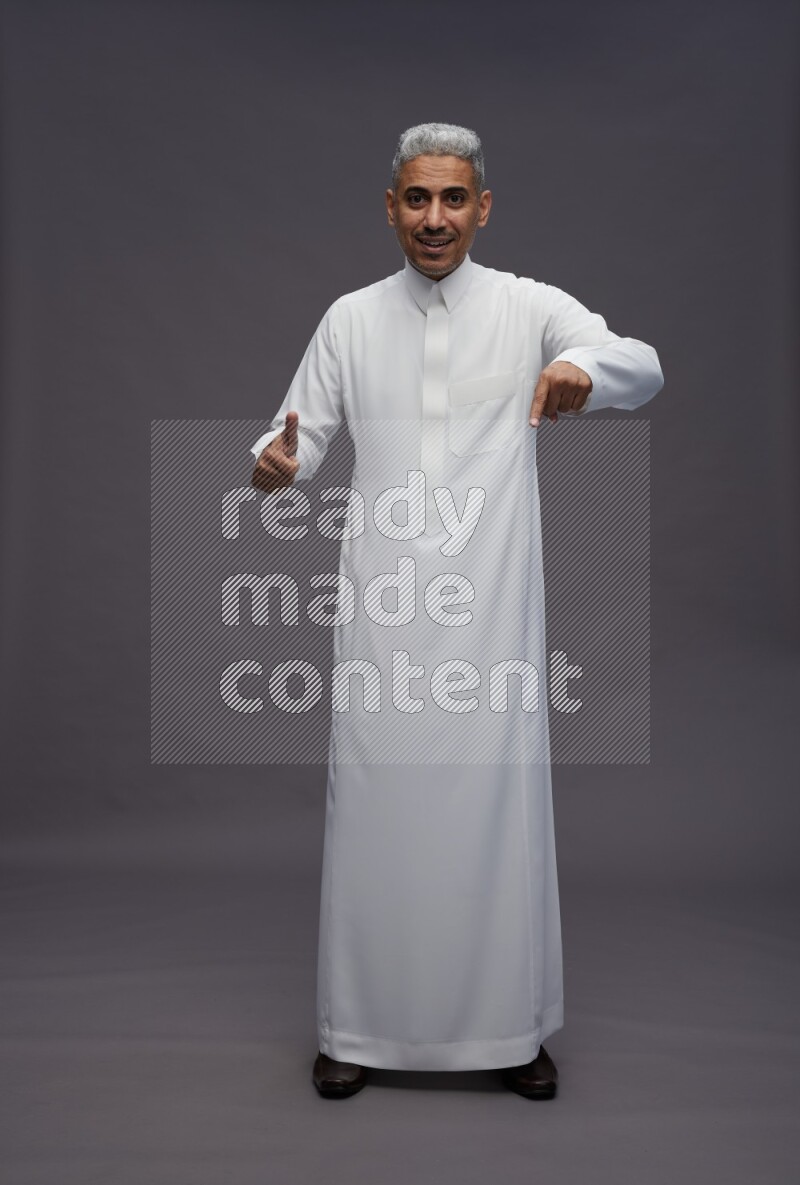 Saudi man wearing thob standing interacting with the camera on gray background