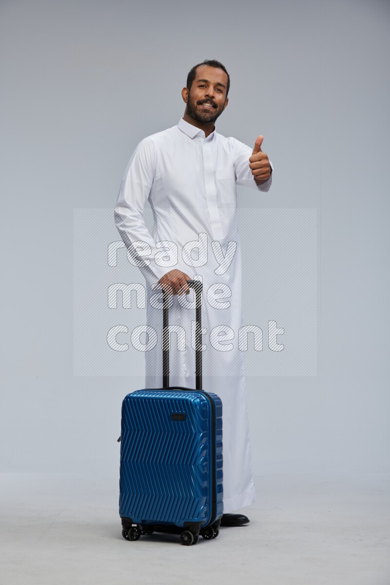 Saudi man wearing thob standing holding Travel bag on Gray background
