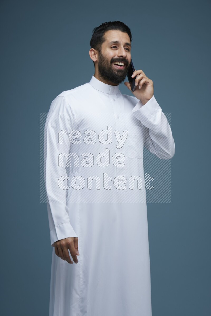 A man having a call on a blue background wearing Saudi Thob
