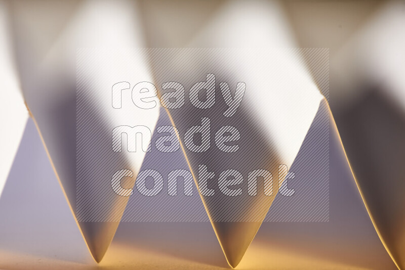A close-up abstract image showing sharp geometric paper folds in white gradients and warm tones