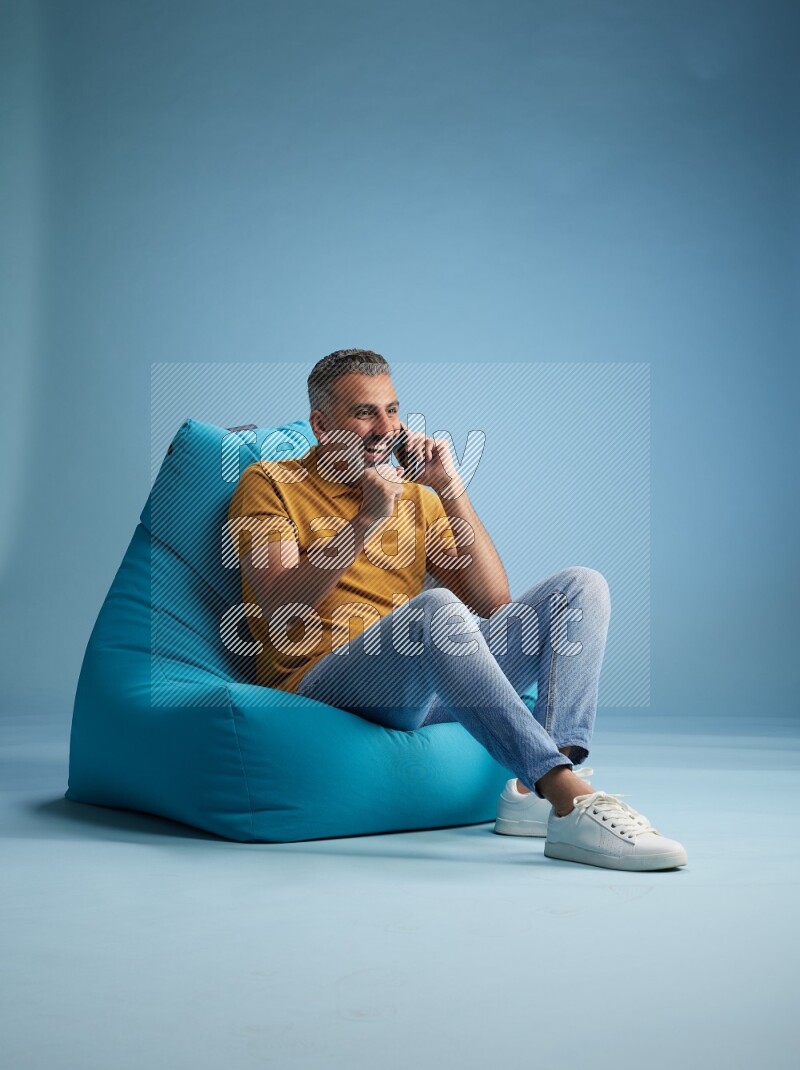A man sitting on a blue beanbag and talking on the phone