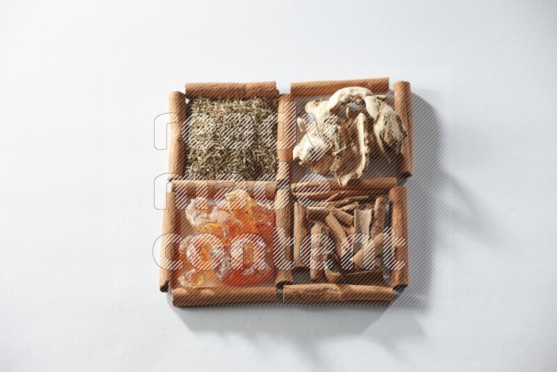 4 مربعات من أعواد القرفة ممتلئة بالكمون والقرفة والزنجبيل المجفف والصمغ العربي على أرضية بيضاء