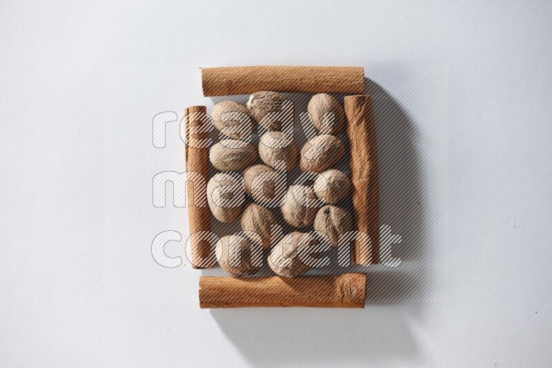 أربعة من أعواد القرفة مكونة شكل مربع بداخلها جوزة الطيب علي خلفية بيضاء