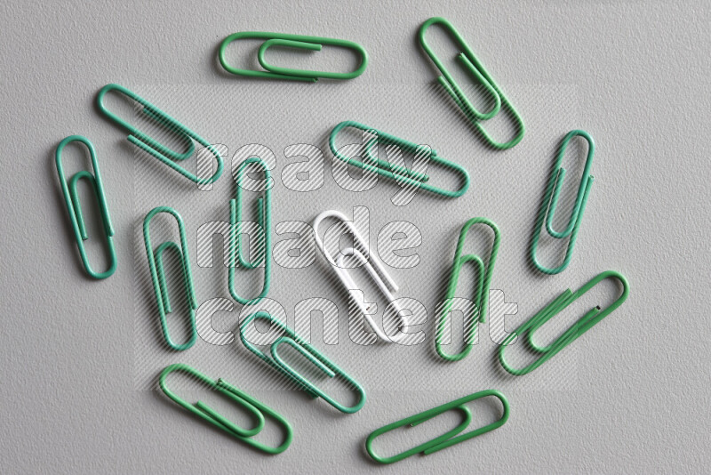 A bunch of green paper clips with a different colored paper clip in the center on grey background