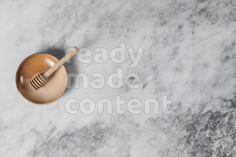 Multicolored pottery plate with wooden honey dipper in it on grey marble background