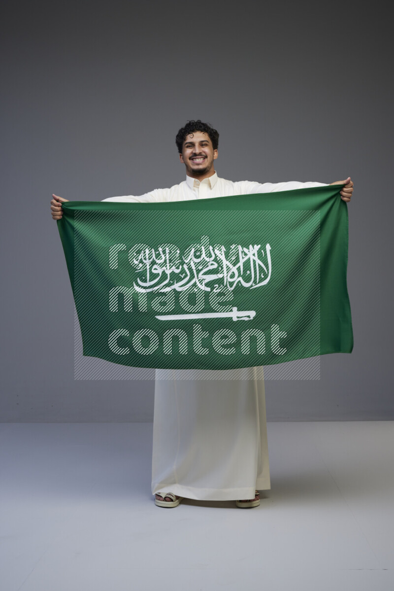 رجل سعودي يرتدي ثوب ويحمل علم السعودية