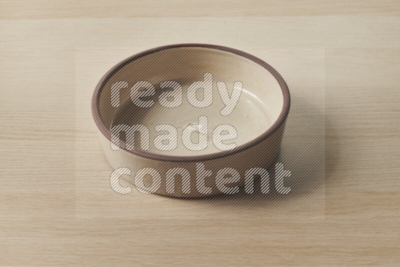 A beige pottery oven bowl on light wooden background