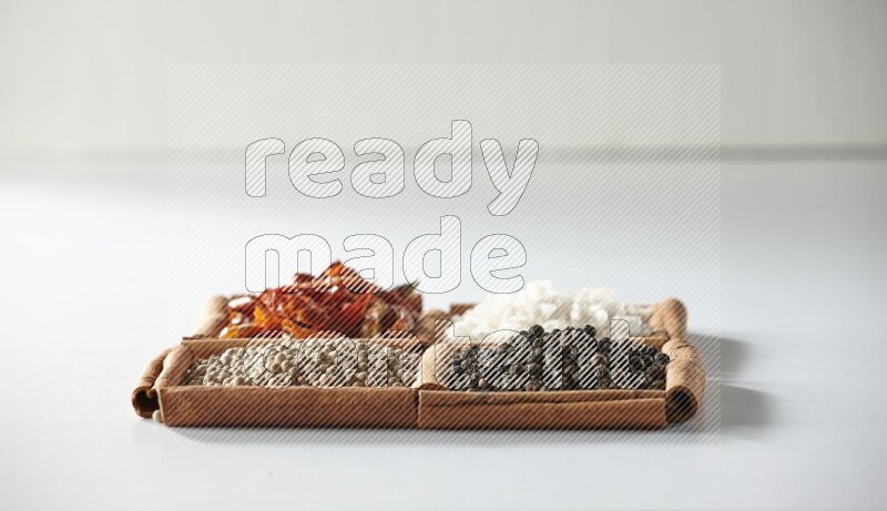 4 مربعات من أعواد القرفة ممتلئة بالفلفل الأحمر والملح والفلفل الأبيض والفلفل الأسود على أرضية بيضاء