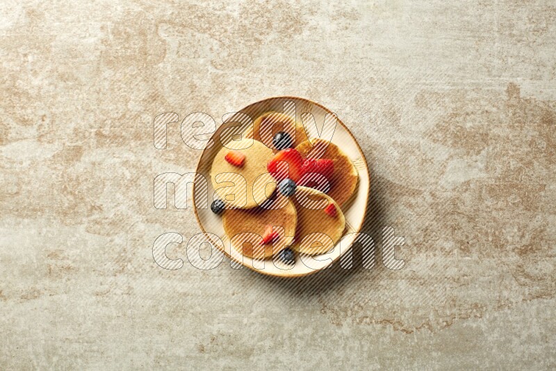 Five stacked mixed berries mini pancakes in an irregular plate on beige background