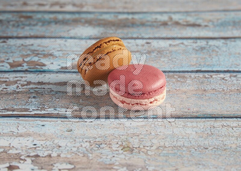 45º Shot of of two assorted Brown Irish Cream, and Pink Litchi Raspberry macarons on light blue background
