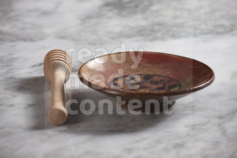 Decorative pottery plate with wooden honey dipper on the side on grey marble background