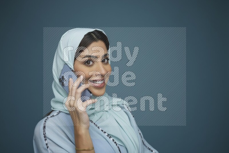 A Saudi woman having a Call in a blue background wearing blue Abaya with hijab