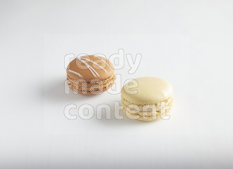 45º Shot of of two assorted Brown Irish Cream, and Yellow Vanilla macarons on white background