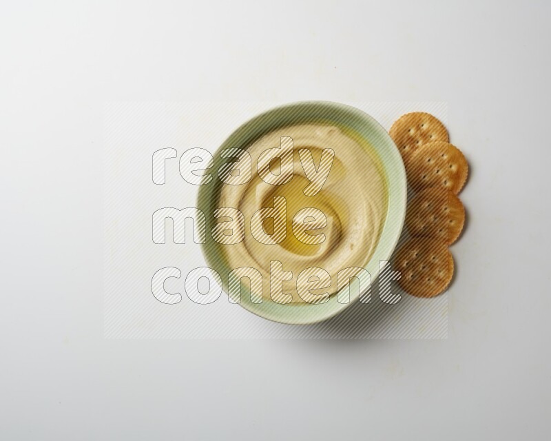 Hummus in a green plate garnished with olive oil on a white background