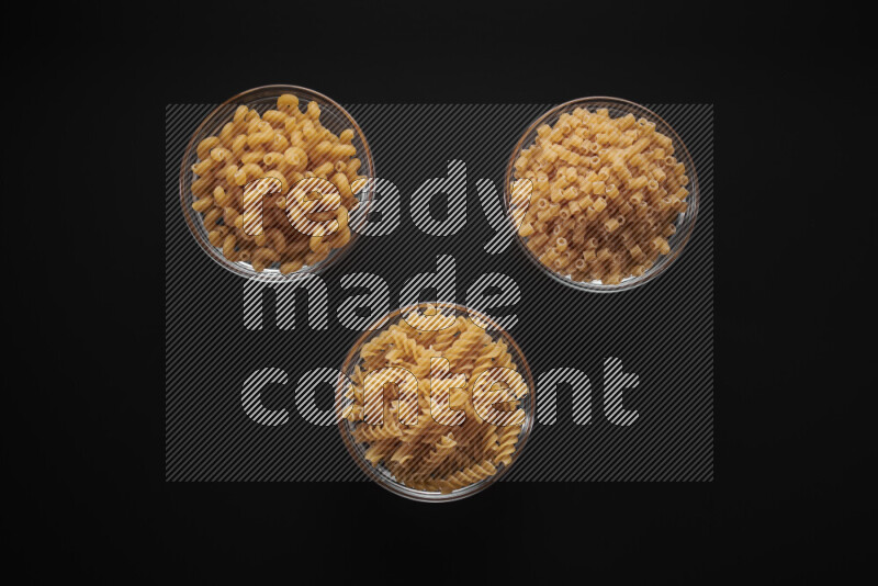 Different pasta types in glass bowls on black background
