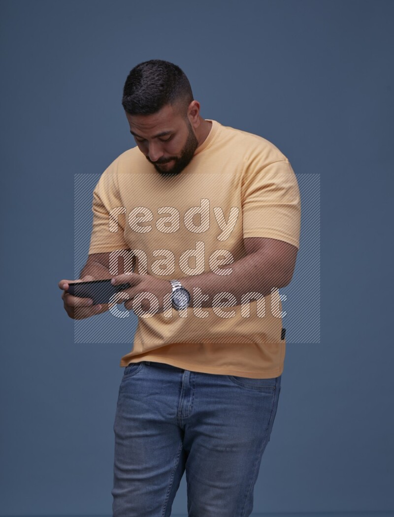 A man Playing Games on Smartphone on Blue Background wearing Orange T-shirt