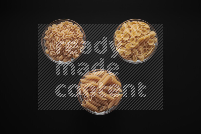 Different pasta types in glass bowls on black background