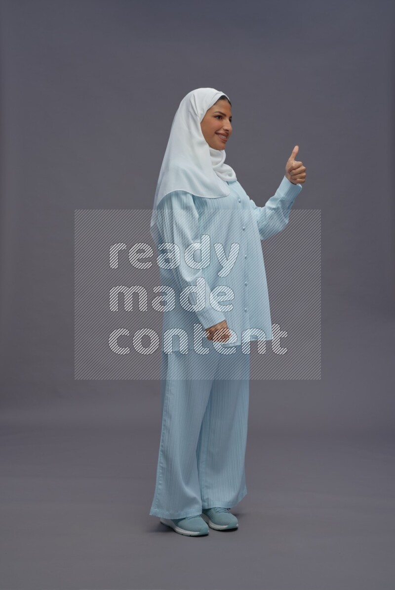 Saudi woman wearing hijab clothes standing interacting with the camera on gray background