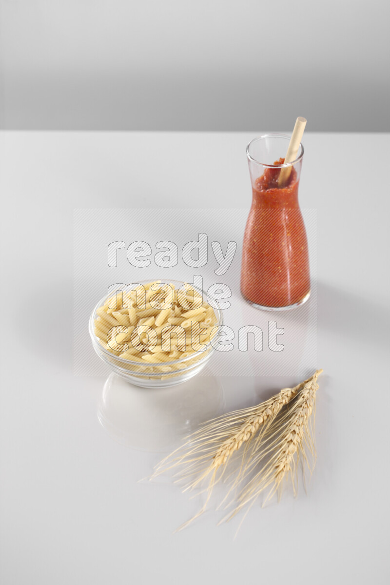 Raw pasta with tomatoe pasta with different ingredients such as cherry tomatoes, basil, garlic, bay laurel, cardamom, white pepper, black pepper, red chilis and wheat stalks on light grey background