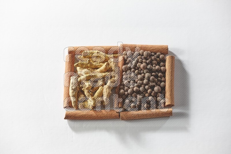 مربعان من أعواد القرفة ممتلئان ببهار الفلفل الحلو وأصابع الكركم علي خلفية بيضاء