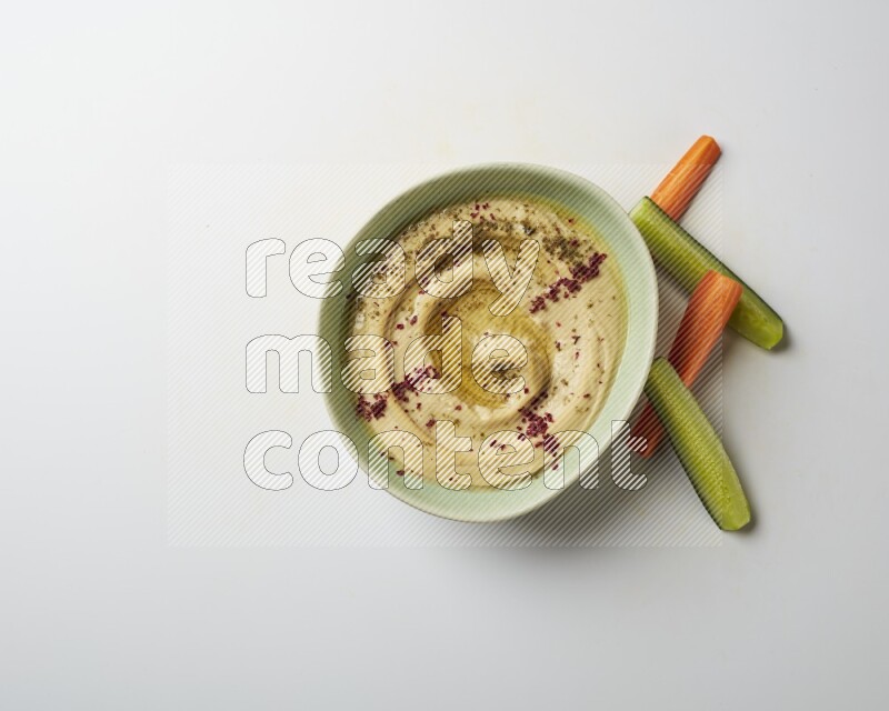 Hummus in a green plate garnished with zattar & sumak on a white background