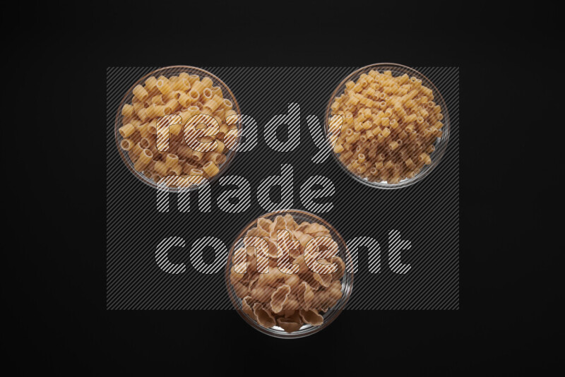 Different pasta types in glass bowls on black background