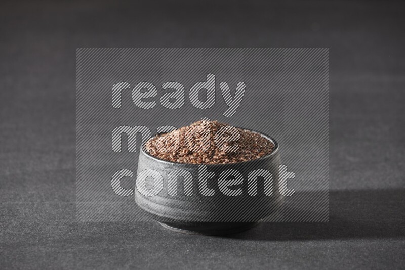 A black pottery bowl full of flaxseeds on a black flooring