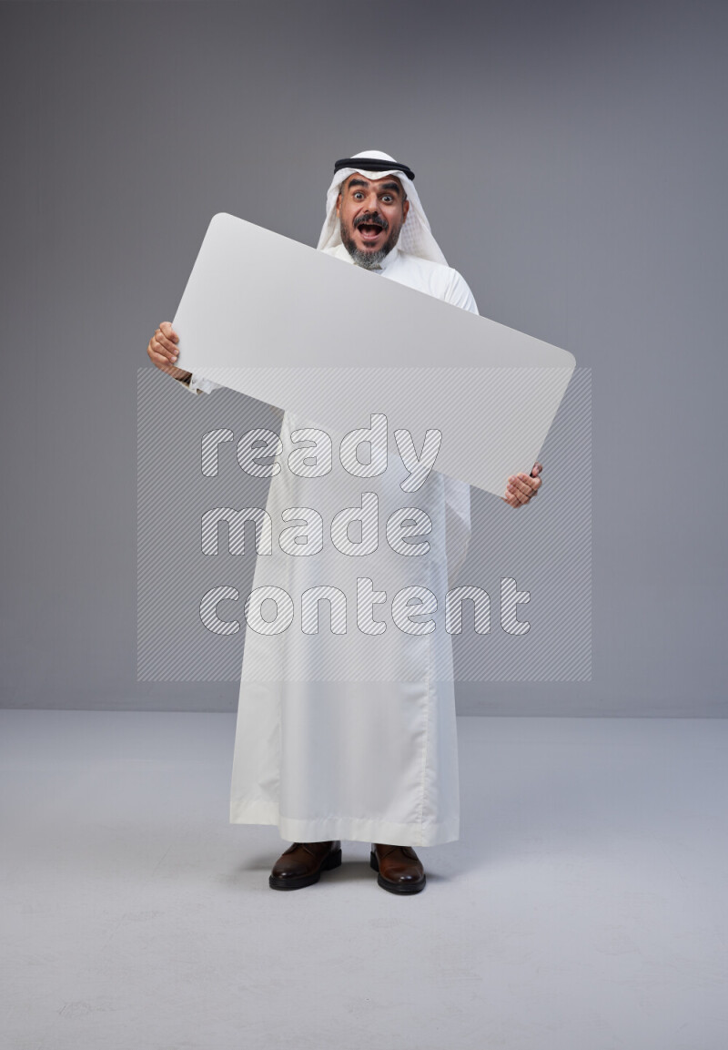 Saudi man Wearing Thob and white Shomag standing holding board on Gray background