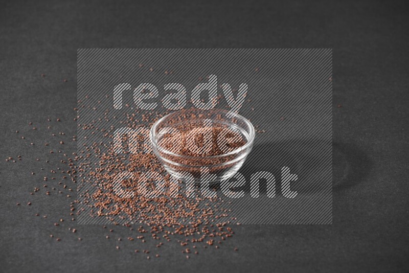 وعاء زجاجي ممتلئ ببذور حب الرشاد محاط بالبذور على أرضية سوداء